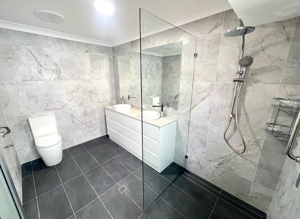 A modern ensuite bathroom that features a walk-in shower with a glass wall panel, rain shower, and double vanity
