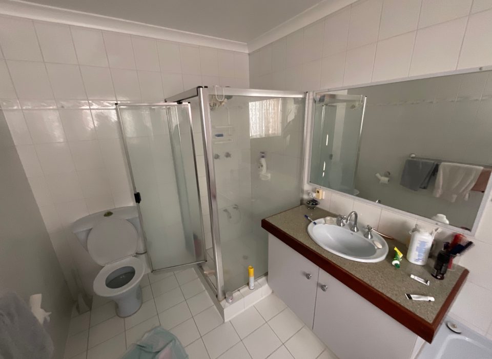 An old bathroom with a glass shower enclosure, single sink and large mirror