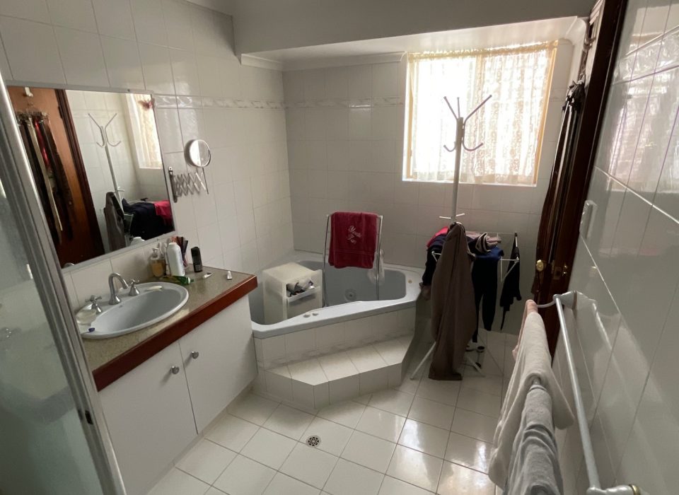 An old bathroom with a spa bath tub and vanity with a single sink and large mirror