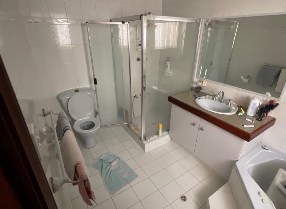 An old bathroom with a glass shower enclosure, single sink and large mirror