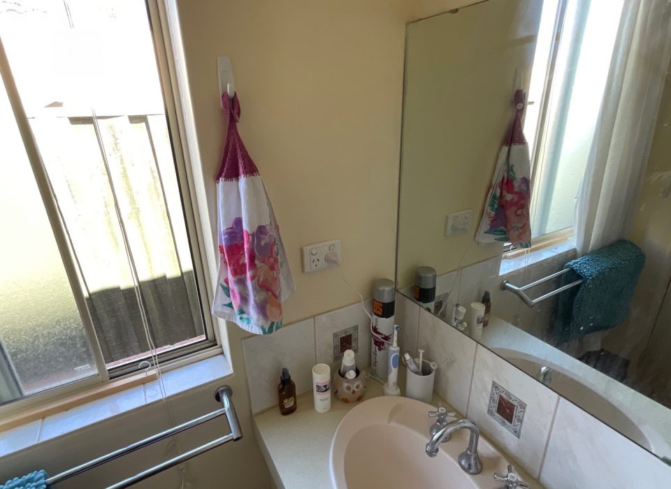 The client's old bathroom, which features a sliding window and vanity with a dated sink and frameless mirror