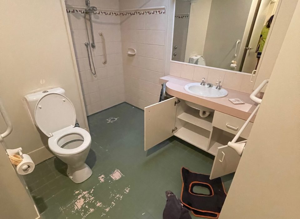 An old bathroom with scuffed green tiles and a dated pink and cream vanity