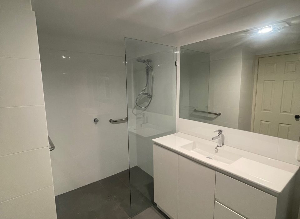 A modern renovated bathroom with dark gray matte floor tiling, an all-white vanity, walk-in shower, and large mirror