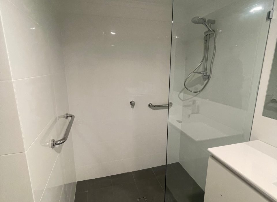A modern renovated bathroom with dark gray matte floor tiling, an all-white vanity, walk-in shower, and large mirror