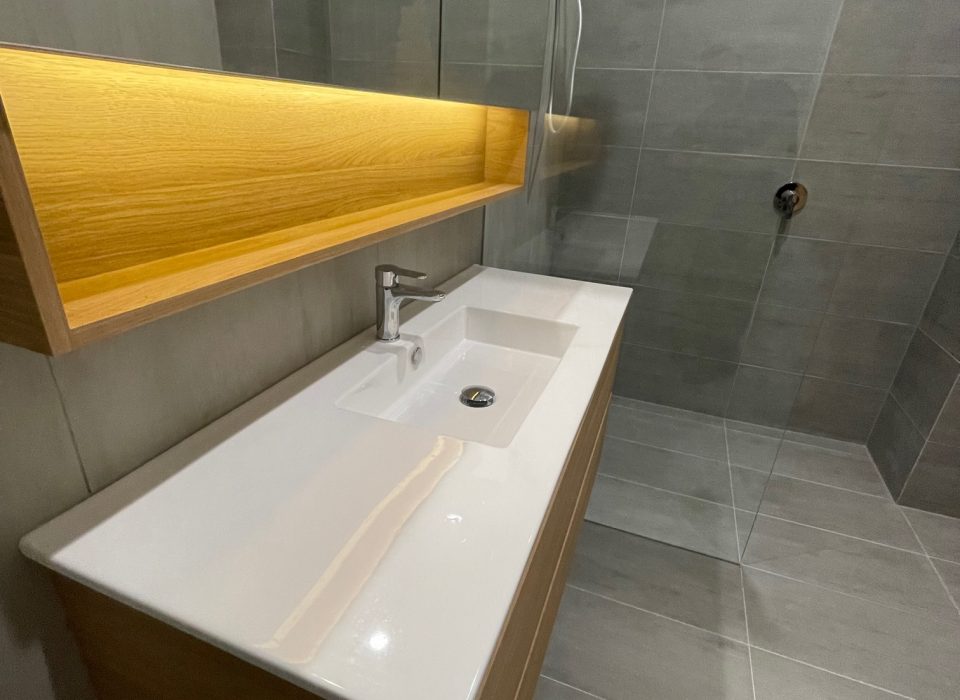 A modern bathroom with a walk-in shower, floating vanity with a large mirrored cabinet, chrome tapware, and large grey floor and wall tiling