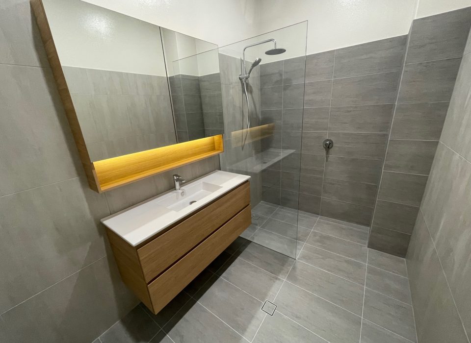 A modern bathroom with a walk-in shower, floating vanity with a large mirrored cabinet, chrome tapware, and large grey floor and wall tiling