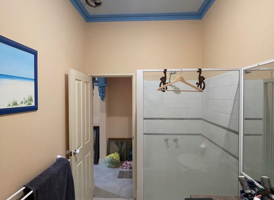 An old bathroom with a shower enclosure, small vanity, and light yellow painted walls