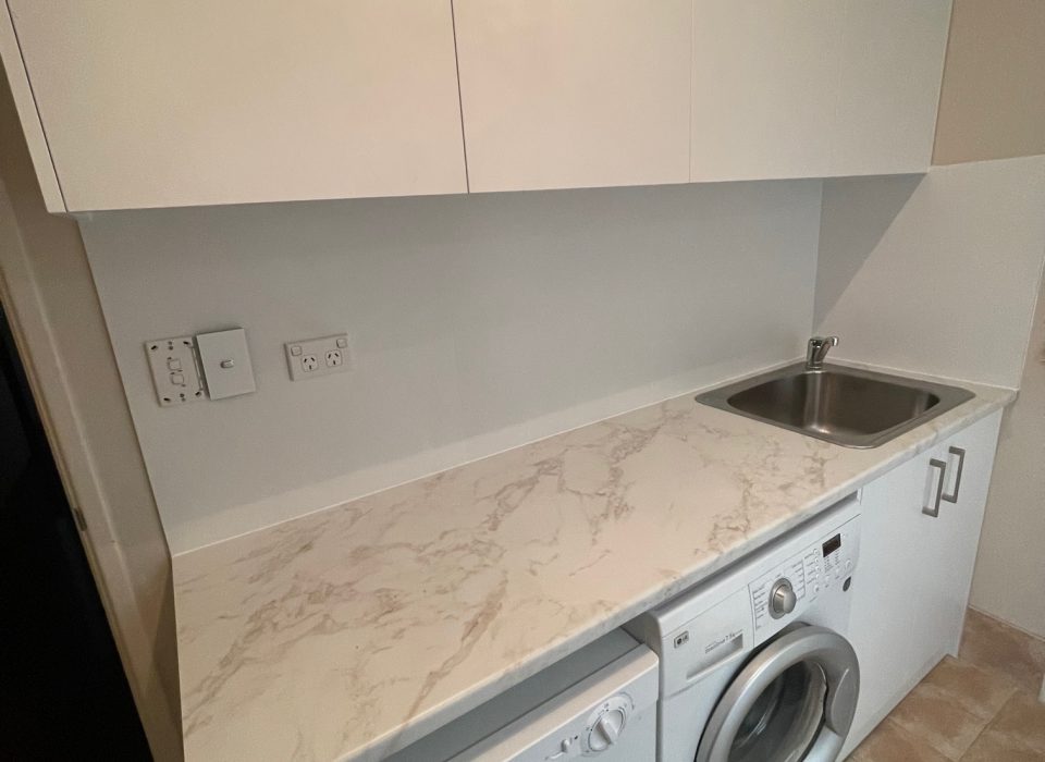 A renovated laundry which features a washer and dryer tucked underneath a marble countertop